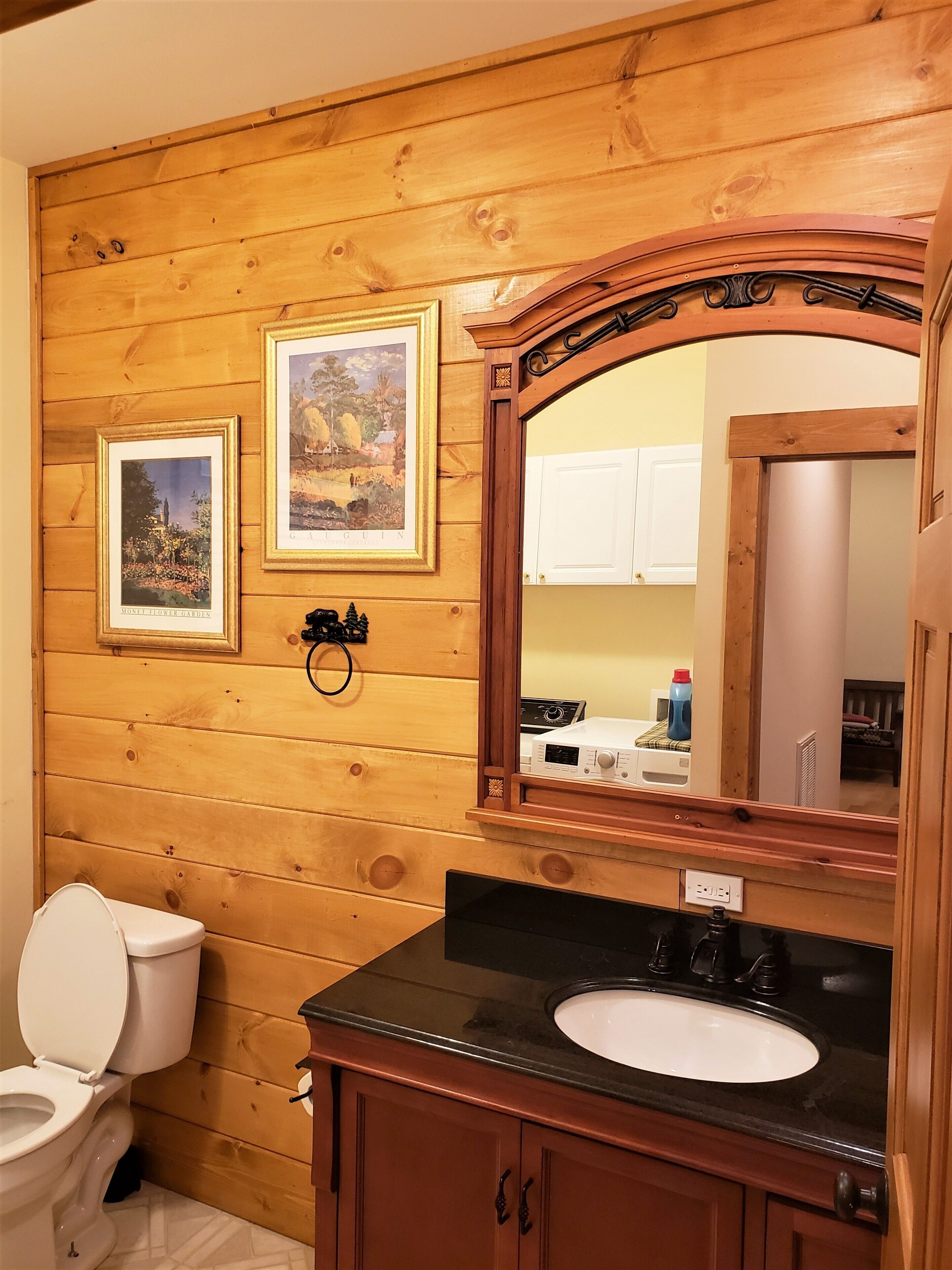 A bathroom with wooden paneling, a white toilet, a black sink, and two framed pictures on the wall.