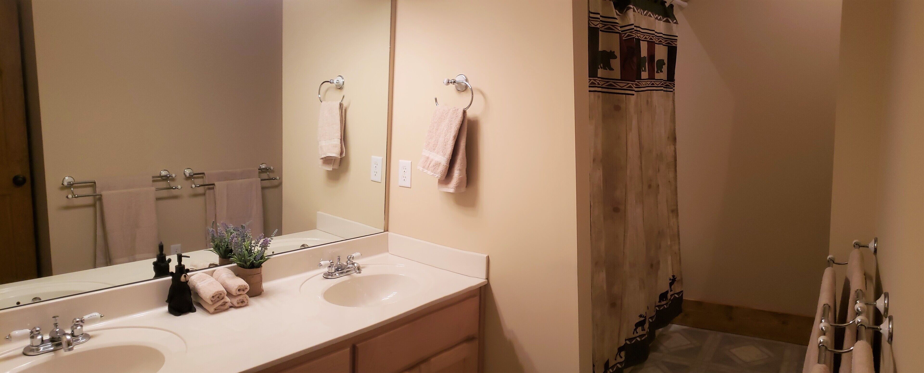 Une salle de bain avec deux lavabos, un miroir et un rideau de douche à motifs animaliers.