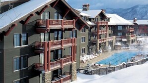 Un hôtel à plusieurs étages doté de balcons, d’un espace piscine et entouré d’un paysage enneigé.