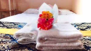 Een net opgemaakt bed met opgevouwen witte handdoeken en een bloemenboeket op het bed.