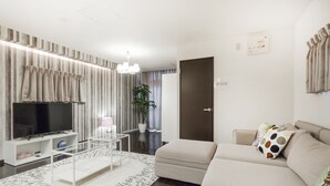 A modern living room with a flat-screen TV, a sofa, a coffee table, and a potted plant. - Crice Hotel (Osaka)