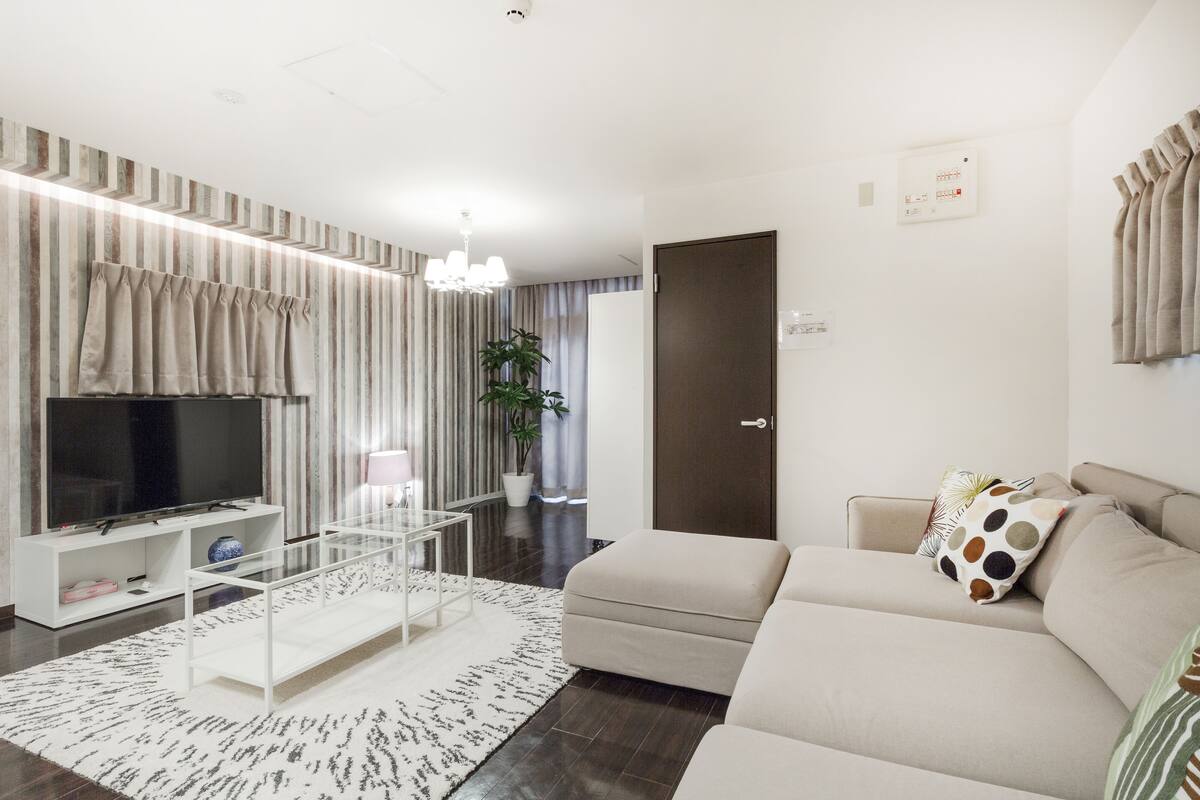 A modern living room with a flat-screen TV, a sofa, a coffee table, and a potted plant.