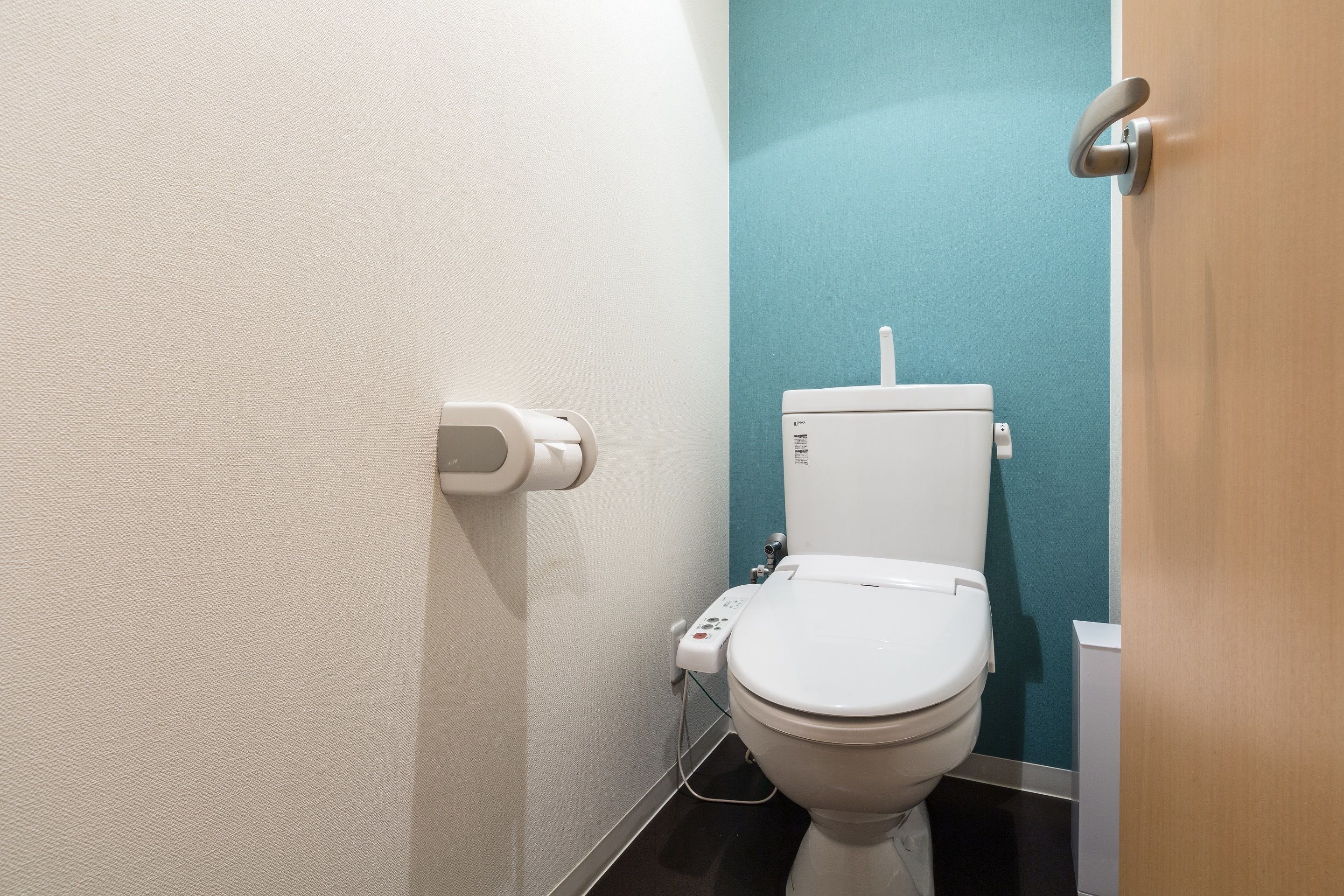 A modern bathroom with a toilet, a paper towel dispenser, and a hand dryer.