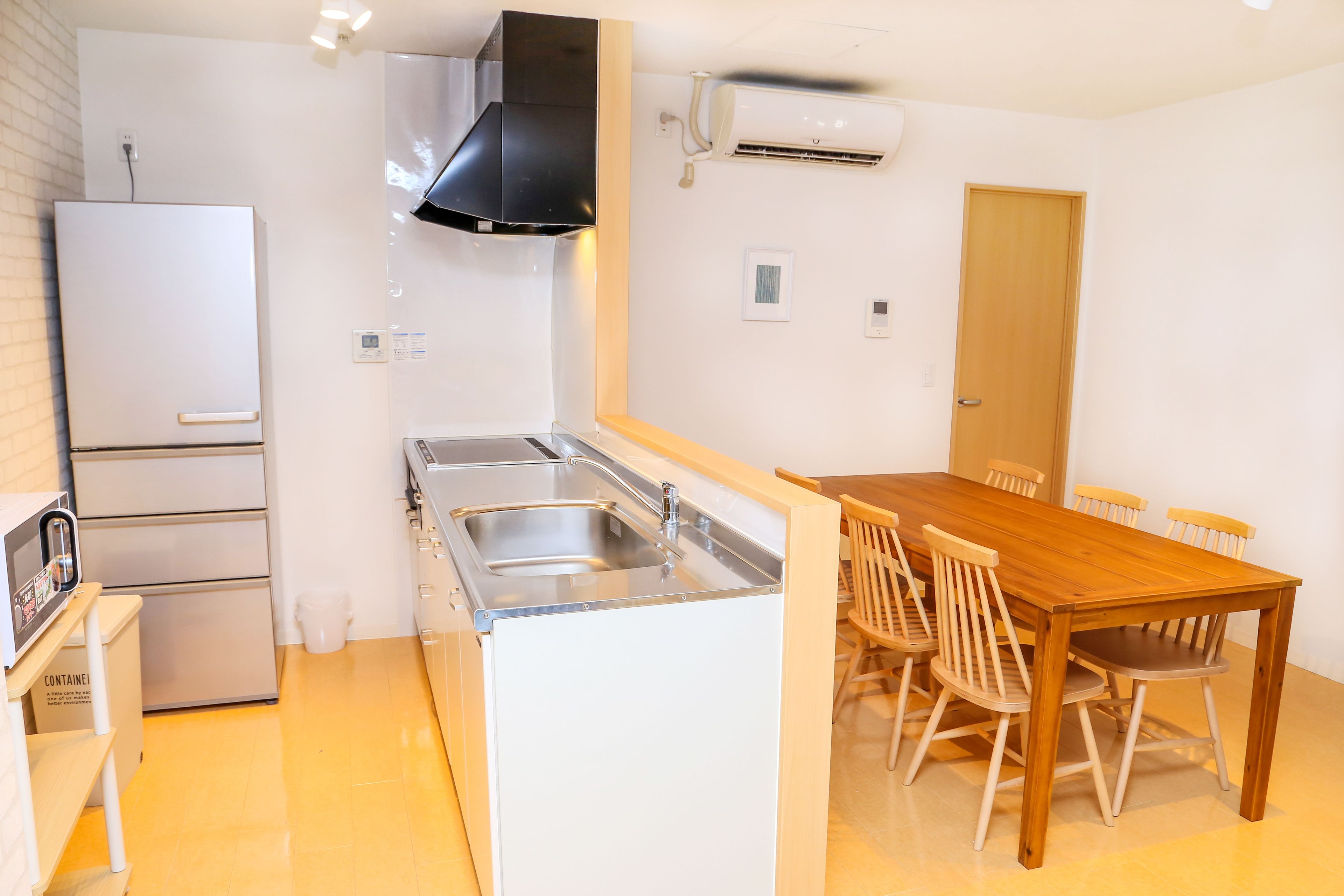 A compact kitchen with a refrigerator, stove, sink, and wooden dining table with chairs.