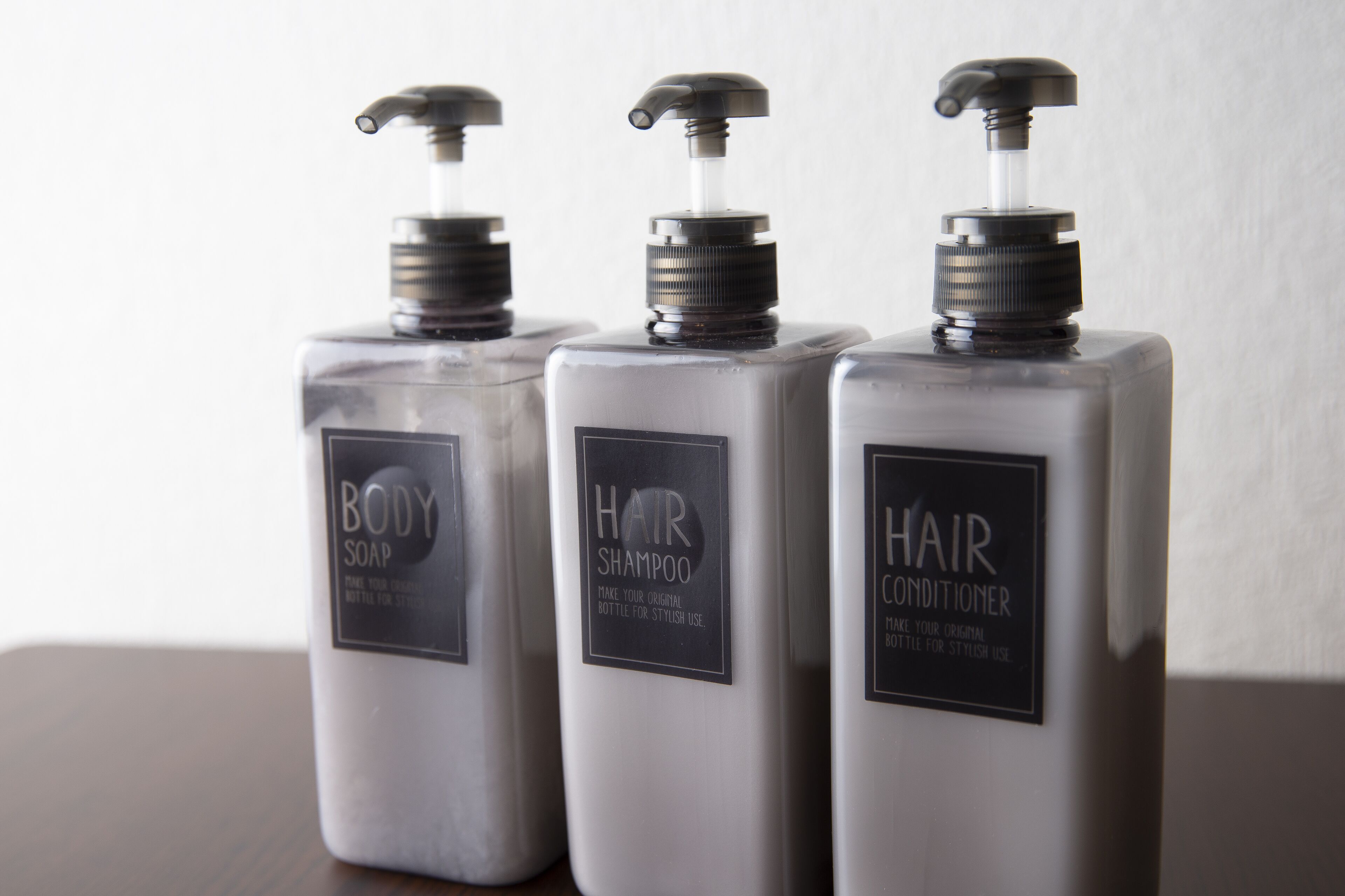 Three bottles of body soap, hair shampoo, and hair conditioner on a table.