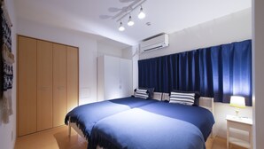 A bedroom with two beds, a wardrobe, an air conditioner, and a bedside table with a lamp. - Crice Hotel (Osaka)