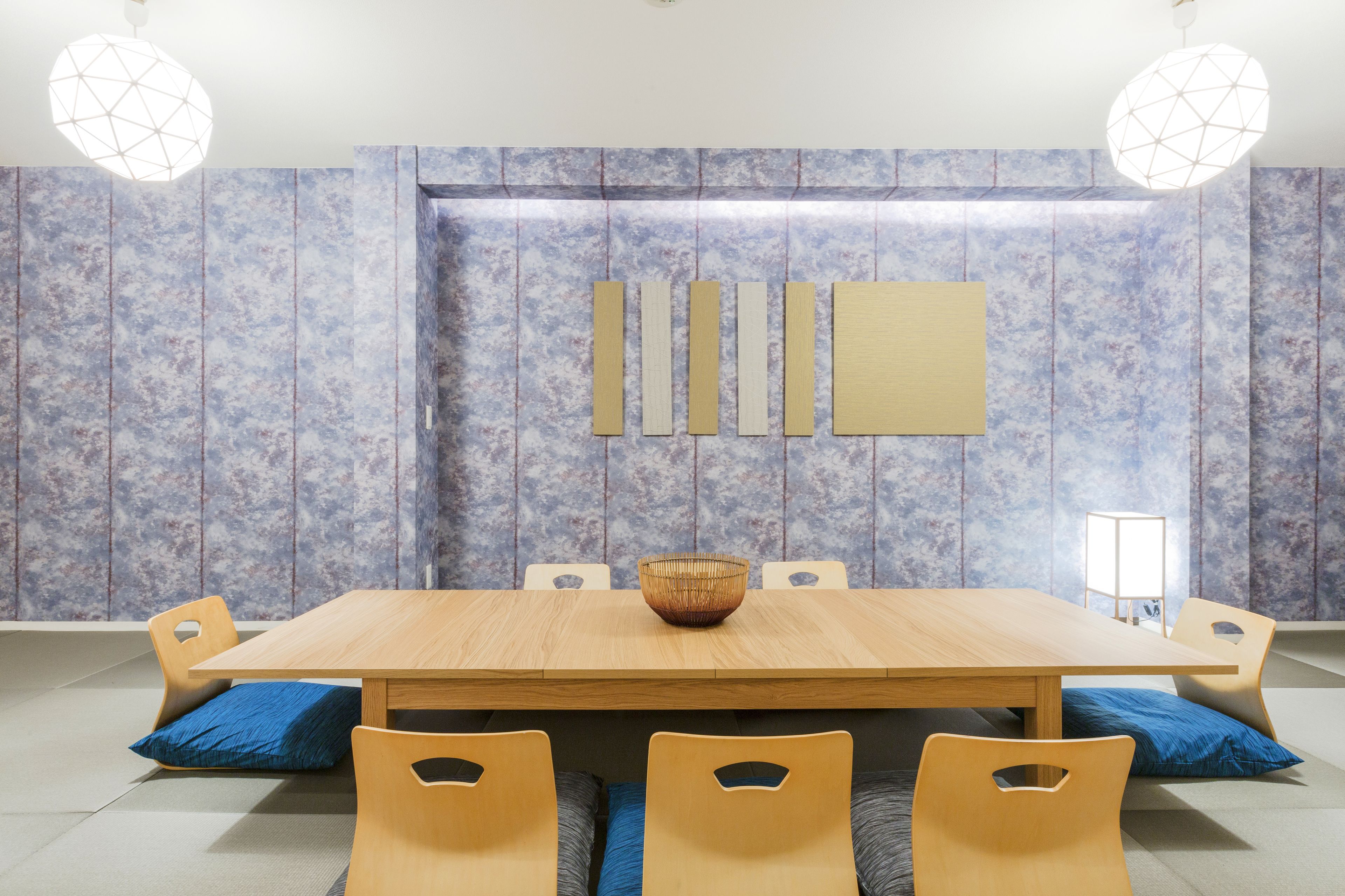 Un espace repas avec une table en bois, des coussins bleus et un luminaire au design géométrique.