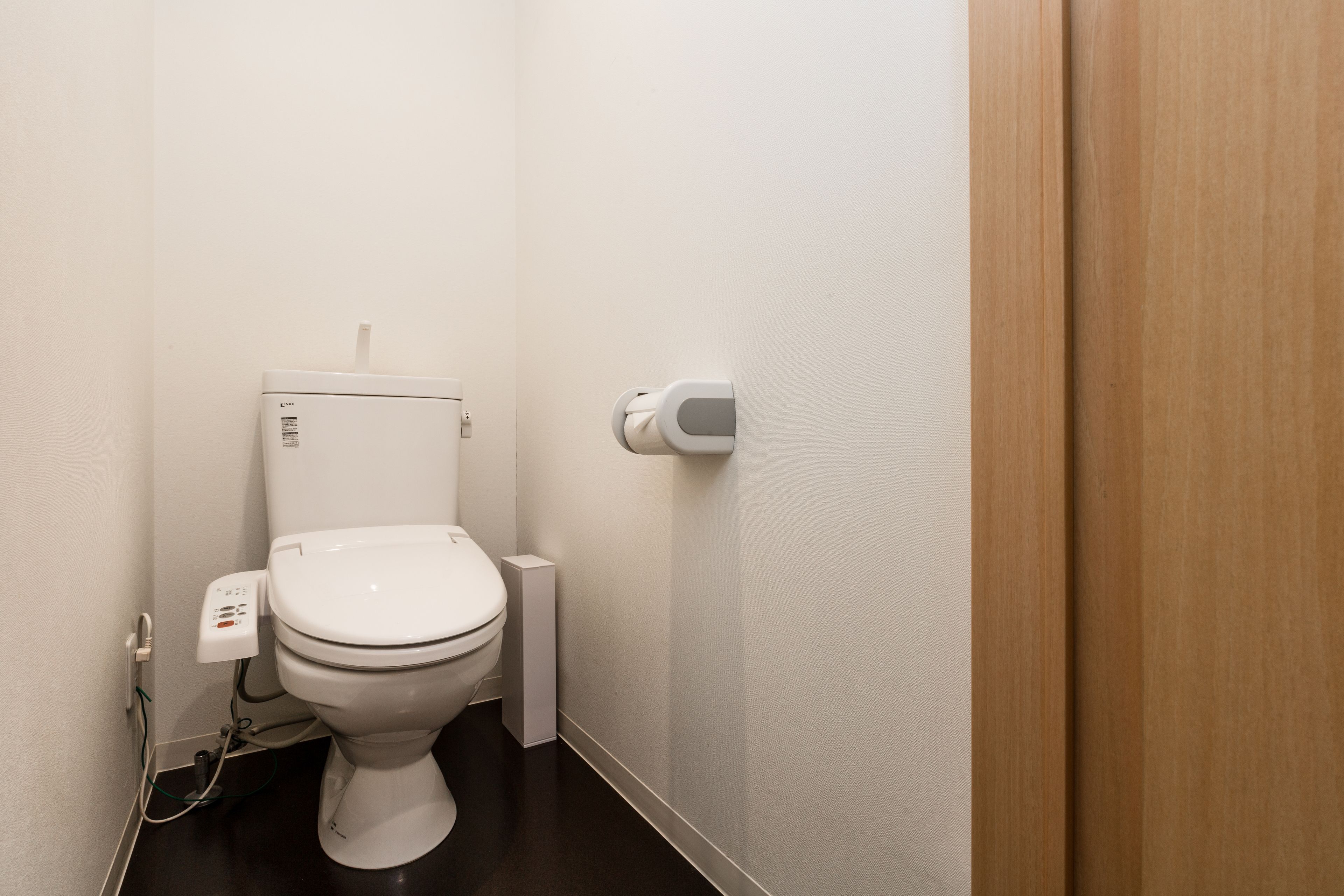 Un baño pequeño y moderno, con inodoro blanco, secamanos y un enchufe visible.