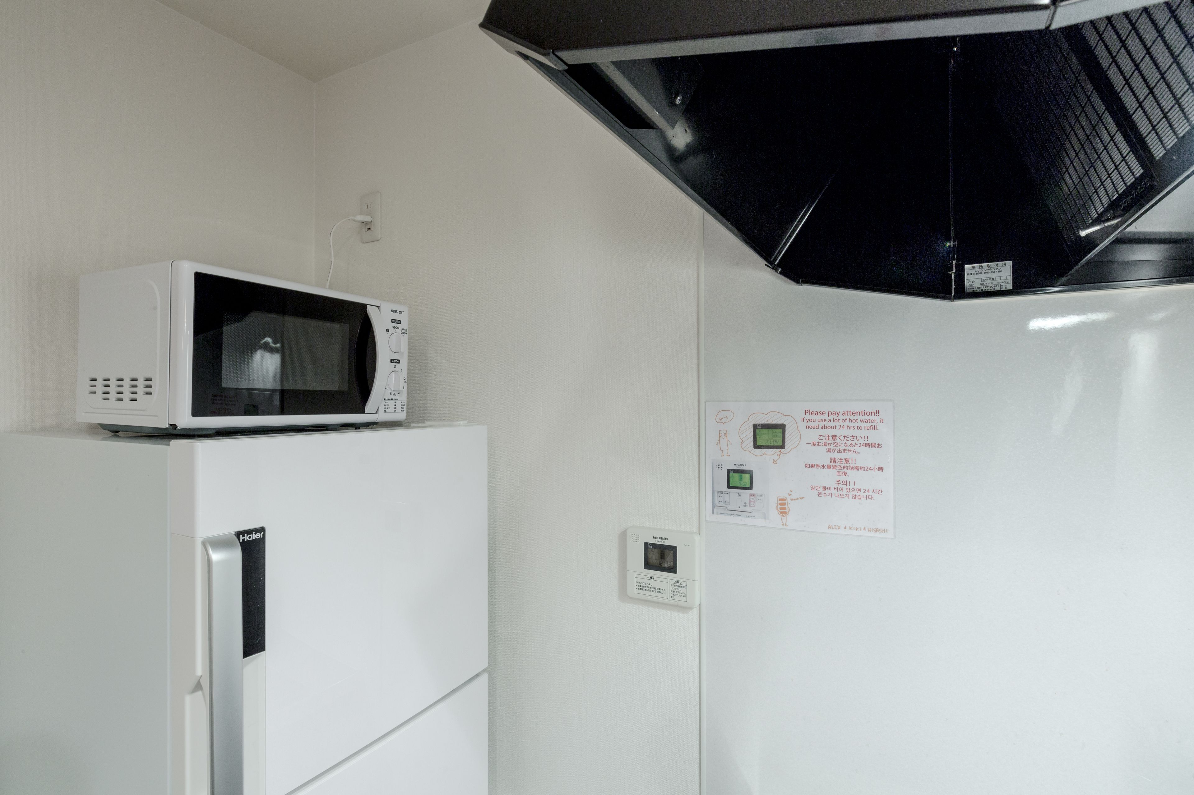 A white refrigerator with a microwave on top, a thermostat, and a notice on the wall.