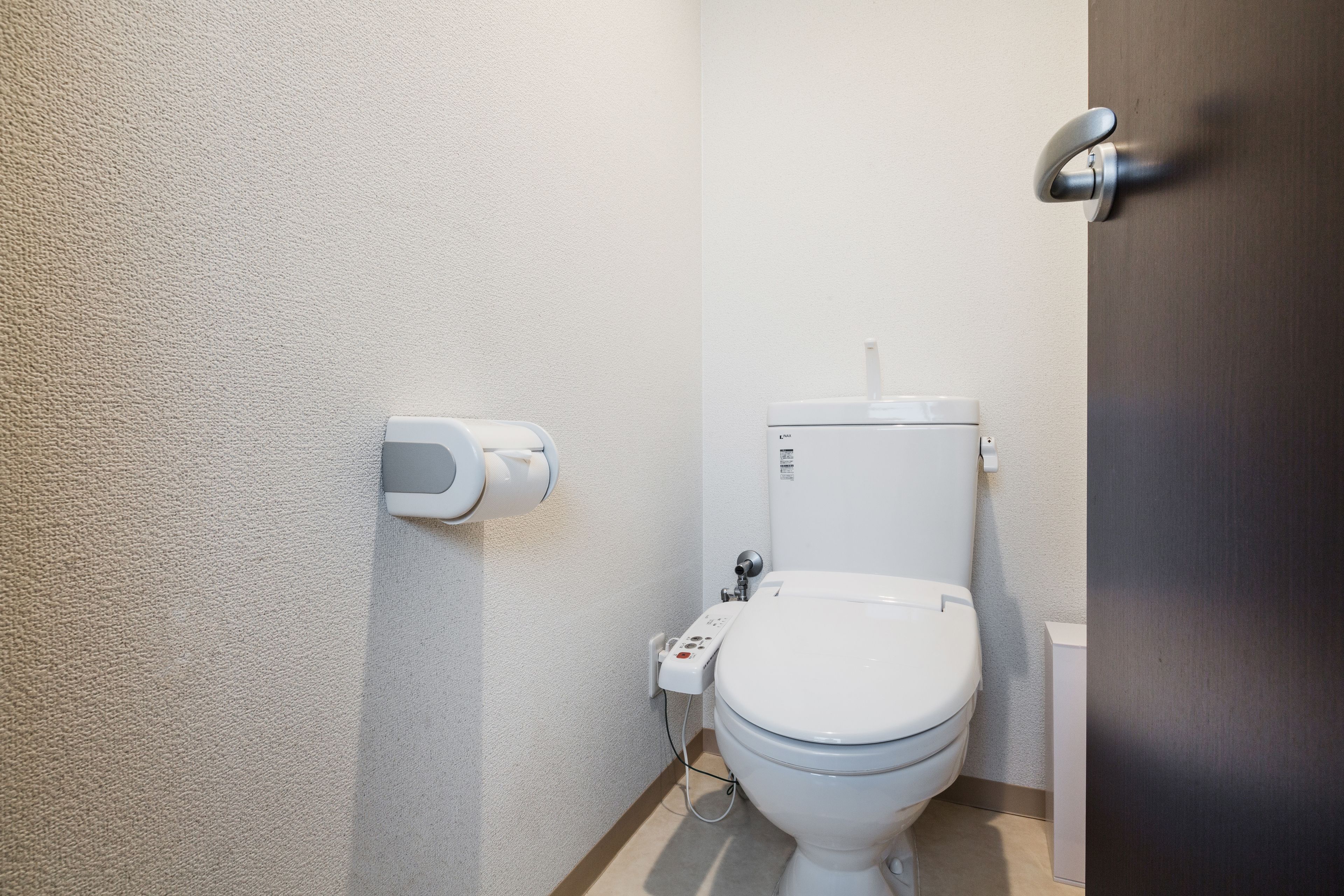 A small, modern bathroom with a white toilet, a hand sanitizer dispenser, and a plain wall.