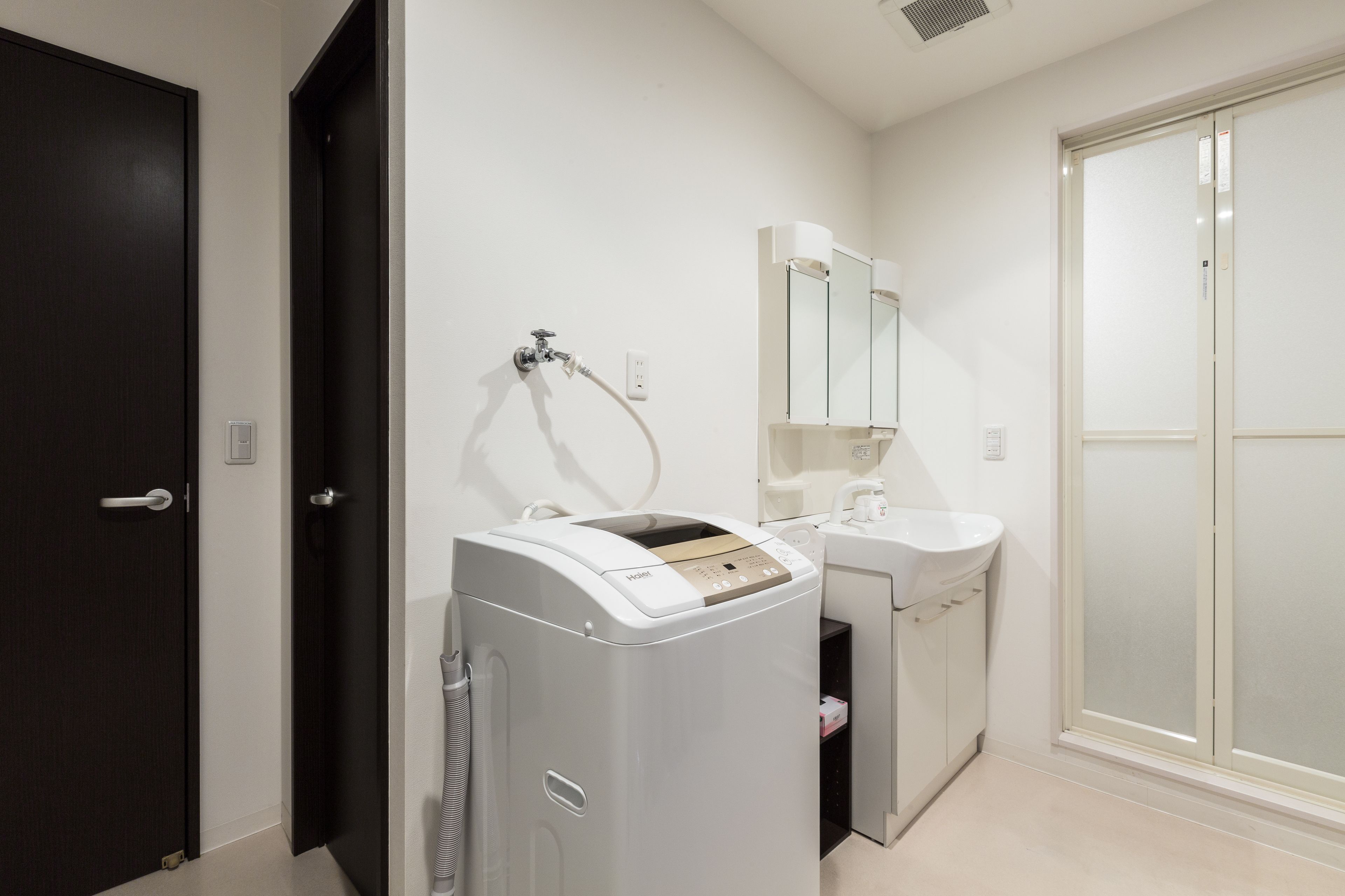 A compact bathroom with a washing machine, a sink, and a glass shower enclosure.