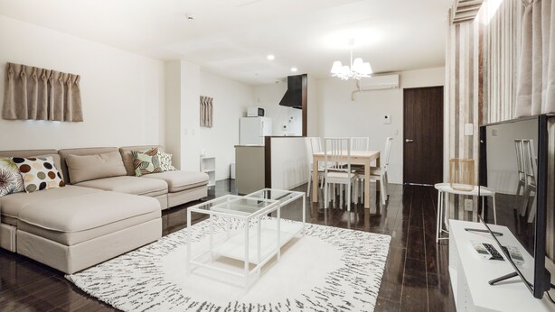 A modern living room with a sofa, coffee table, and dining area. - Crice Hotel (Osaka)