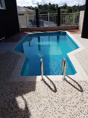 A rectangular swimming pool with tiled edges and metal handrails, surrounded by a tiled deck and a white fence. - F2 ideally located in Guadeloupe (petit bourg)