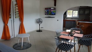 Una zona de menjador amb una taula i cadires, un ventilador i una televisió penjada a la paret.