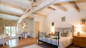 Ein Schlafzimmer mit Bett, Nachttisch, Lampe sowie ein Badezimmer mit Badewanne und Waschbecken.