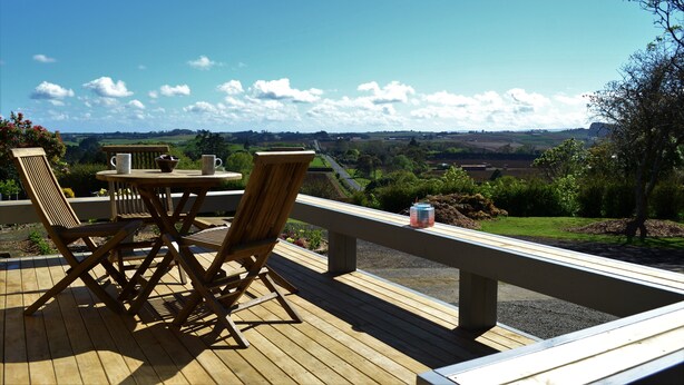 Een houten terras met een tafel en stoelen, met uitzicht op een schilderachtig landschap met heuvels en een heldere lucht.