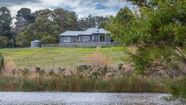 Ett hus med en inhägnad trädgård och en vattenyta i förgrunden.