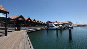 Un muelle frente al agua con un pasillo de madera que lleva a una fila de restaurantes, incluyendo 'DOME' y 'Chill'. Hay barcos amarrados en el agua.