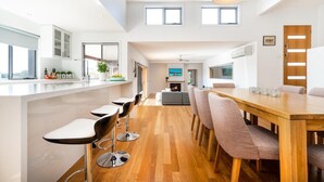 A modern kitchen with a central island, bar stools, and a dining area with a wooden table and chairs. - Highview - LOVE A ROOM WITH A VIEW (Tootgarook)