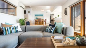 A modern living room with a grey sectional sofa, a wooden coffee table, and a dining area in the background. - Highview - LOVE A ROOM WITH A VIEW (Tootgarook)