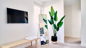 Une pièce dotée d’un grand téléviseur à écran plat fixé au mur, d’un banc en bois, d’un présentoir à miroir avec un cadre photo et d’une plante en pot.