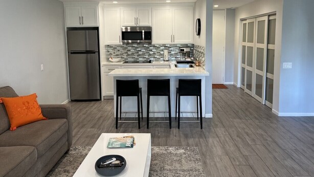 Una cocina moderna con gabinetes blancos, un refrigerador de acero inoxidable y un microondas. Hay una barra con taburetes y una isla grande.