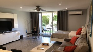 Habitación de hotel moderna con zona de comedor, dos camas, televisor y balcón con vistas.