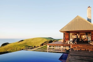A modern building with a wooden deck and an infinity pool overlooking a grassy landscape.