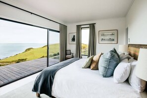 A bedroom with a large bed, a view of the sea, and a wooden deck outside.