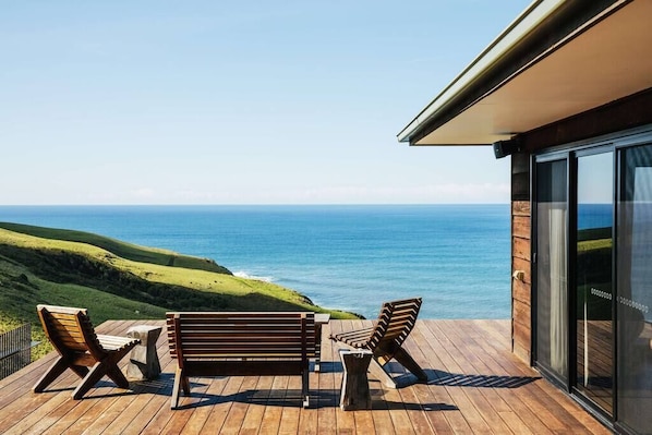 A wooden deck with outdoor furniture overlooking a coastal view.