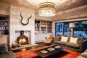 A cozy living room with a fireplace, bookshelves, a sofa, and a large window.