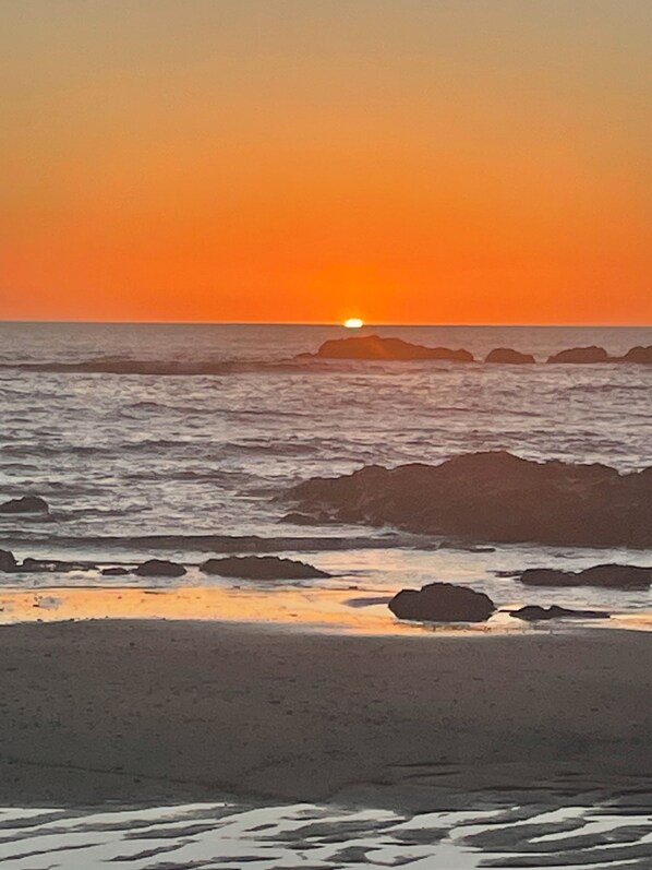 Escena de playa con un atardecer, olas y rocas.
