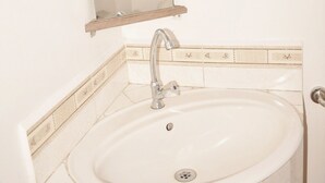 Casa de banho com lavatório branco, espelho e painel de azulejos.