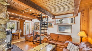 Ein gemütliches Wohnzimmer mit Holzboden, einem braunen Ledersofa, einem Couchtisch aus Holz und einer Wendeltreppe.