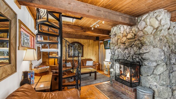 Ein gemütliches Wohnzimmer mit Kamin aus Stein, Holzbalkendecke, einer Ledersofa und einer Wendeltreppe.