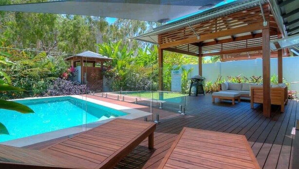 A wooden deck with a pool, lounge chairs, and a pergola.