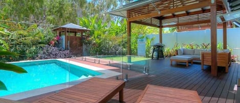 Una terraza de madera con piscina, sillas de descanso y un pérgola.