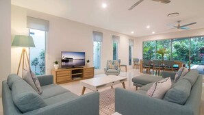 A modern living room with a flat-screen TV, two sofas, a coffee table, and a dining area with a table and chairs.