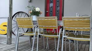 A wooden deck with metal chairs and a table, a red door with the number 110, and a large yellow 'S' sign. - Stylish spacious vintage house, wood fire, 40m to beach inside a National Park (Sisters Beach)