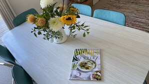 A dining table with a floral centerpiece and a magazine titled "Gourmet Traveller Mediterranean Summer". - Stylish spacious vintage house, wood fire, 40m to beach inside a National Park (Sisters Beach)