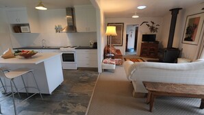 A compact kitchen with white cabinets, a stove, and a microwave. There is a dining area with a sofa and a wooden table. - Stylish spacious vintage house, wood fire, 40m to beach inside a National Park (Sisters Beach)