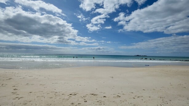 A beach with footprints leading to the water, a clear sky, and a distant landmass. - Stylish spacious vintage house, wood fire, 40m to beach inside a National Park (Sisters Beach)
