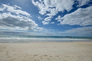 A beach with footprints leading to the water, a clear sky, and a distant landmass.