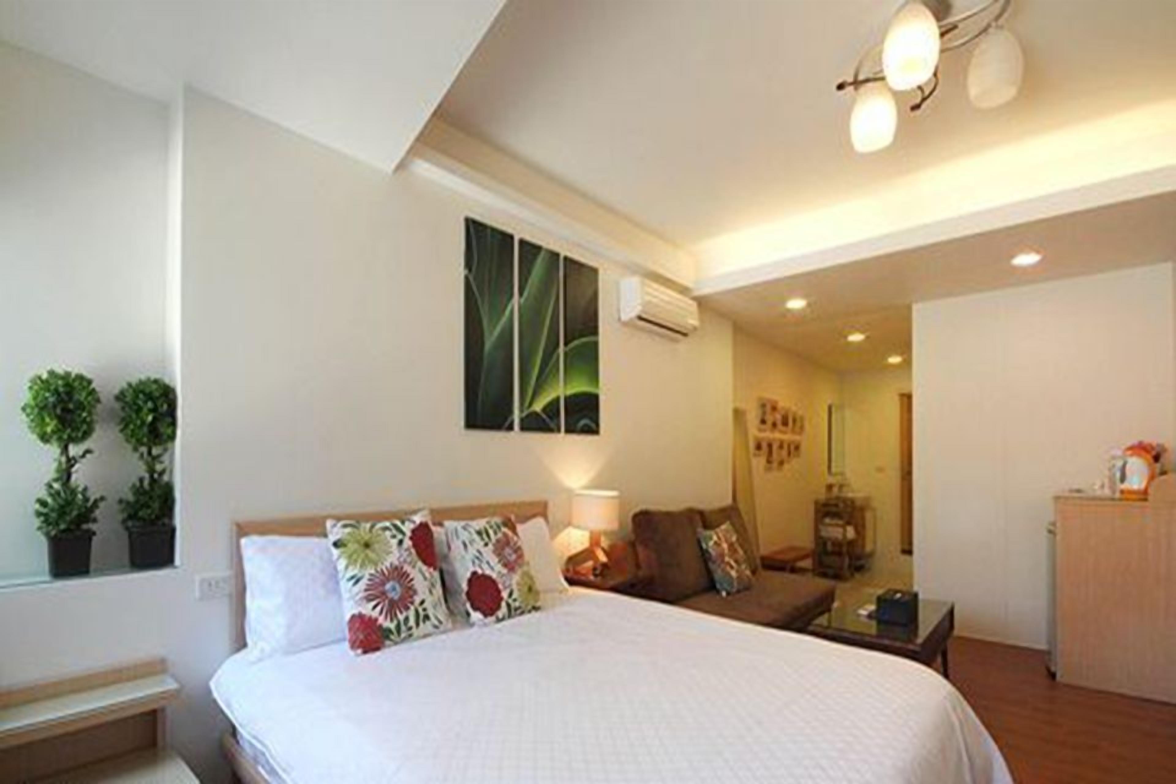 A hotel room with a bed, a desk, a chair, a lamp, and a small cabinet.