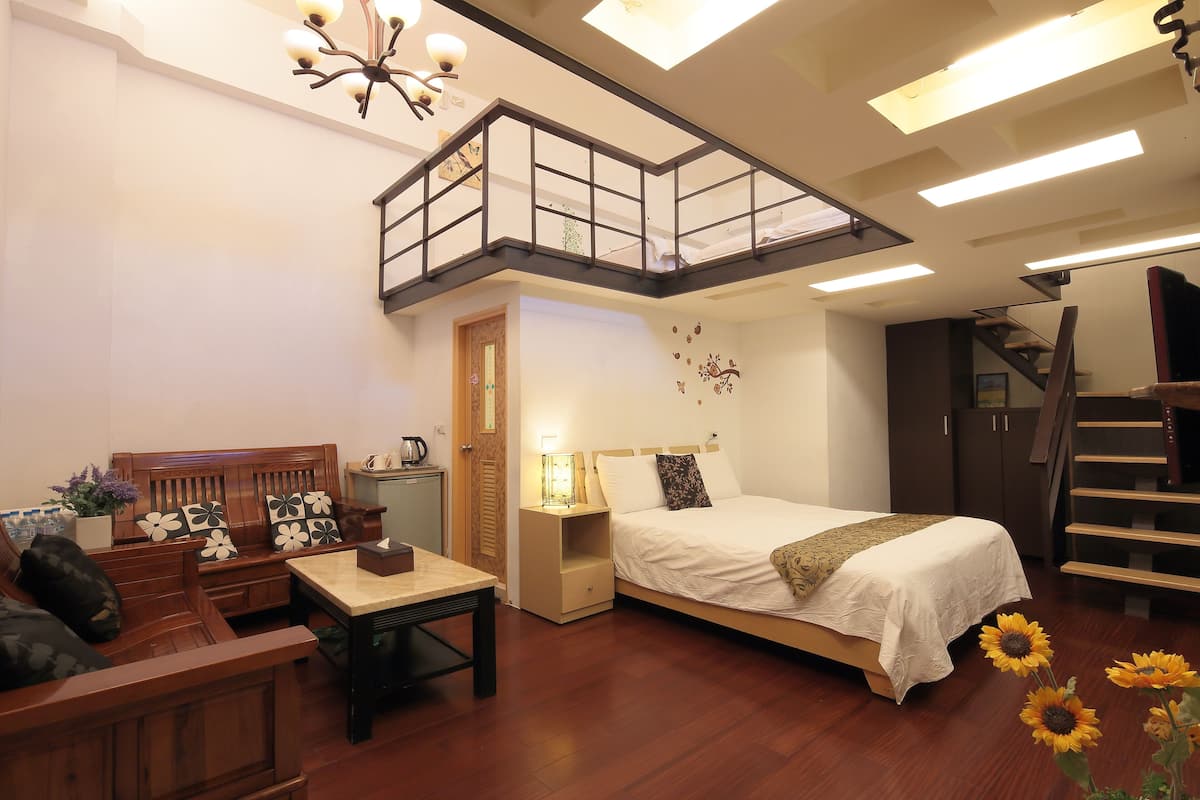 A bedroom with a bed, a wooden bench, a nightstand, a desk, and a staircase.