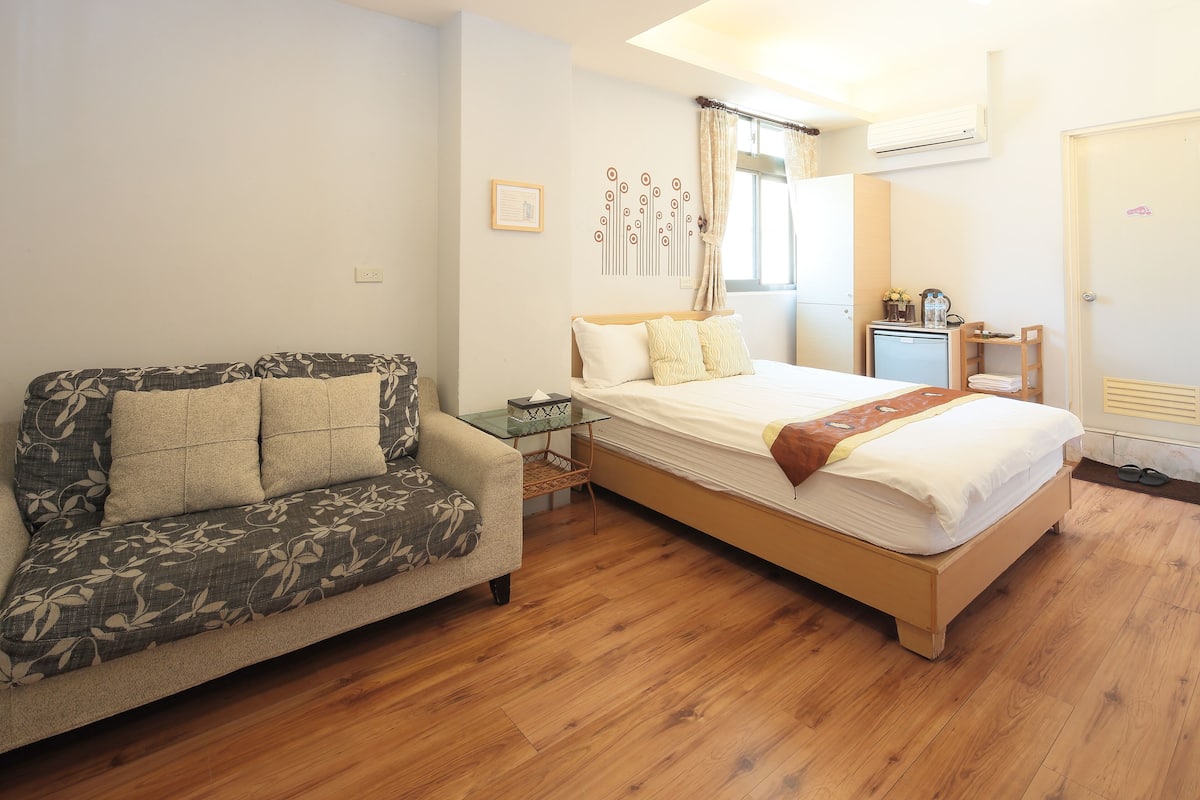 A bedroom with a bed, a sofa, a bedside table, and a small cabinet.