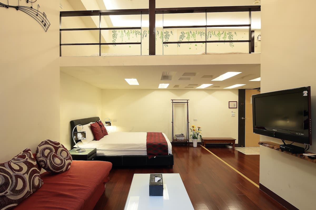 A hotel room with a bed, a sofa, a TV, and a balcony with plants.
