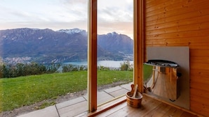 A wooden cabin with a large sliding glass door leading to a balcony, overlooking a mountainous landscape and a lake. - A Place That Stays With You - The Cloud House (bellagio)