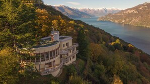 A modern house with a curved roof, surrounded by dense forest and overlooking a lake with mountains in the background. - A Place That Stays With You - The Cloud House (bellagio)