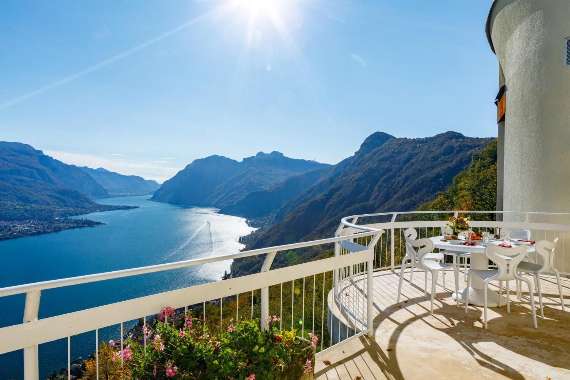 A balcony with a table set for dining, overlooking a mountainous landscape and a body of water.